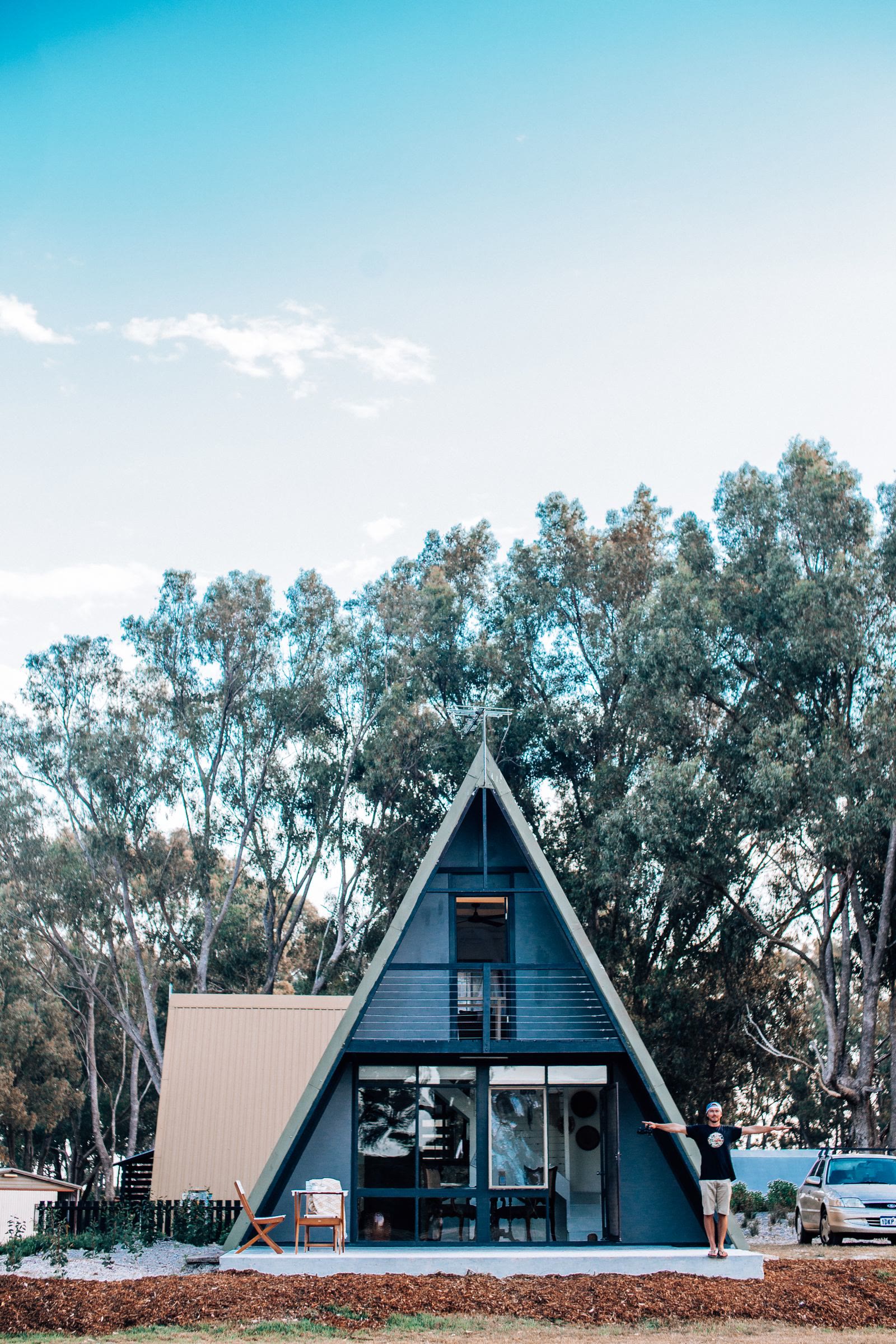 Chalé A-frame azul com fachada de vidro e árvores ao fundo